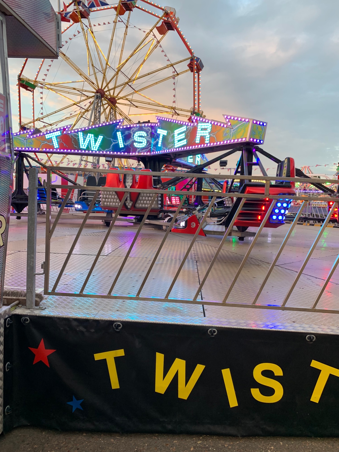 Colourful Twister fairground ride and ferris wheel lit up at dusk